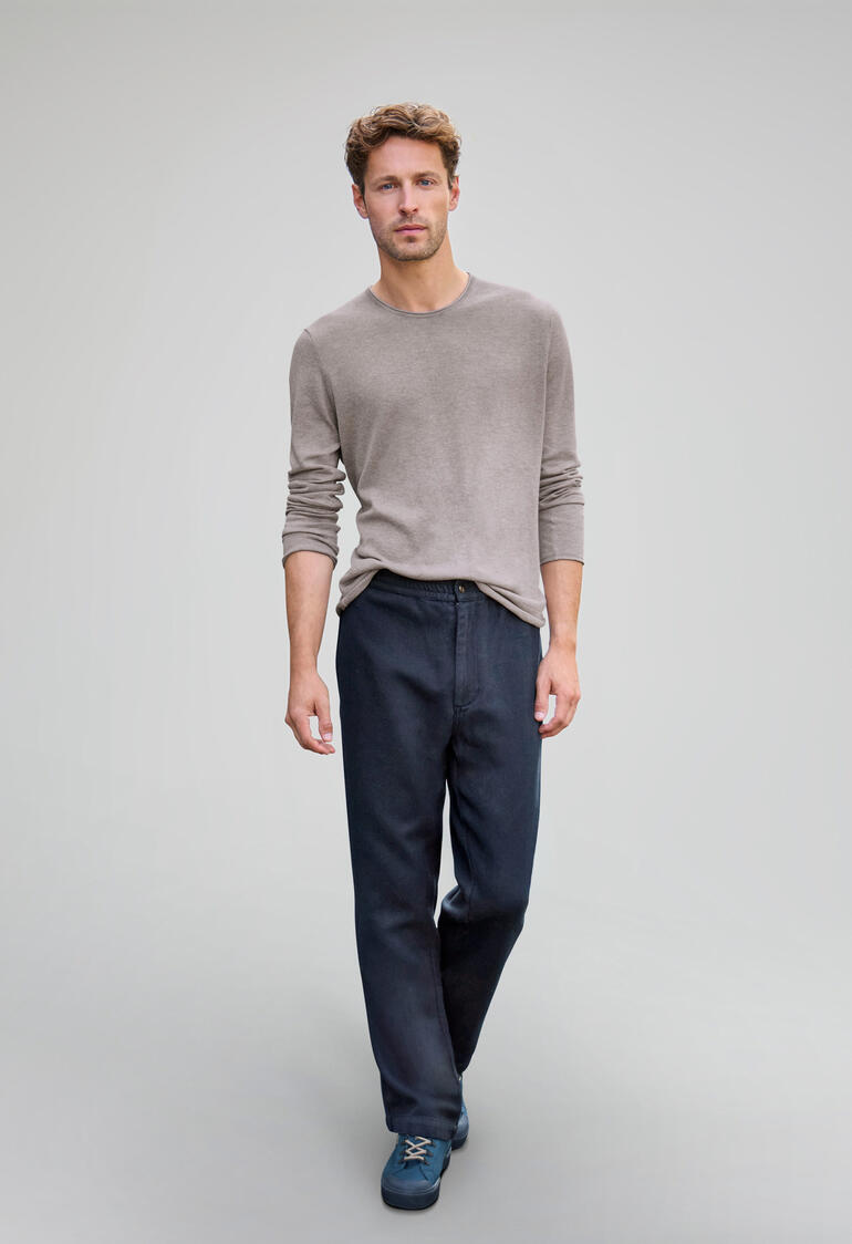 Homme en chemise beige et pantalon navy sur fond gris