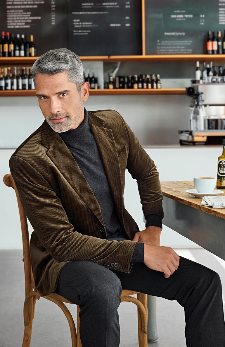 Homme en blazer en corduroy marron assis dans un café avec un look élégant.