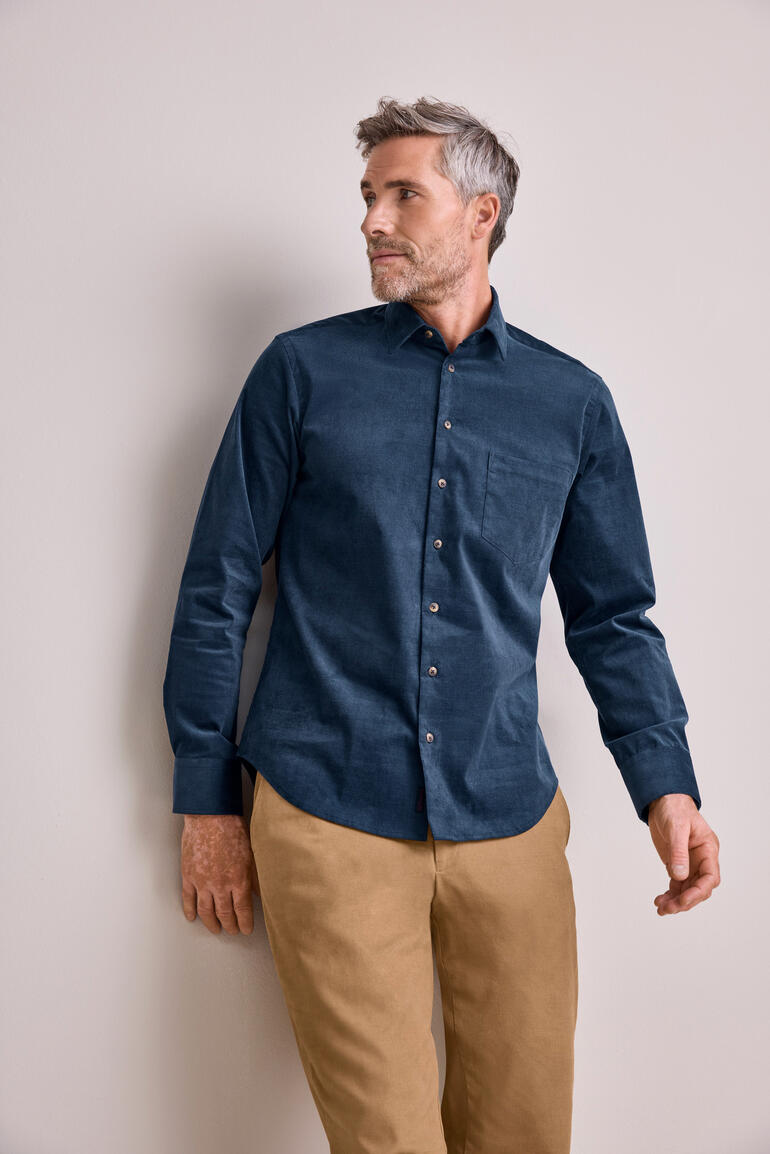 Homme en chemise en velours côtelé bleu marine avec un pantalon beige.