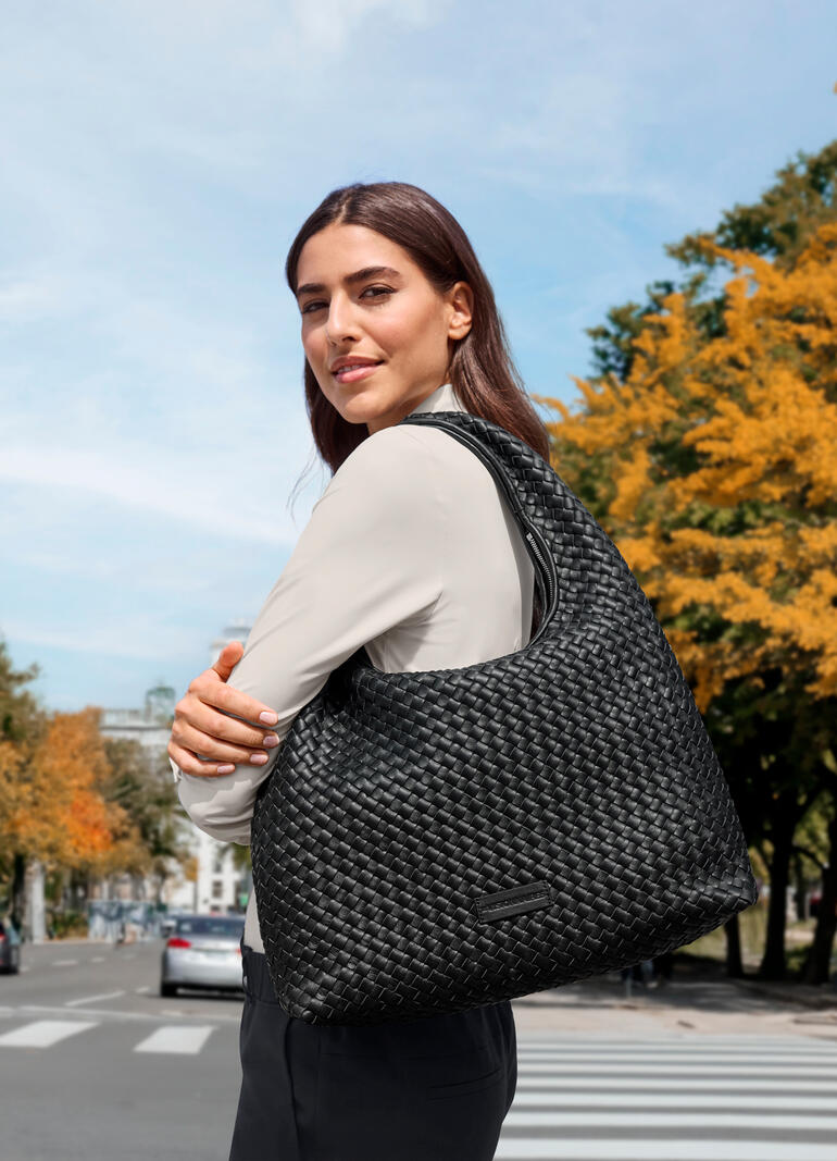 Femme portant un sac Hobo tressé noir sur une rue animée en automne.