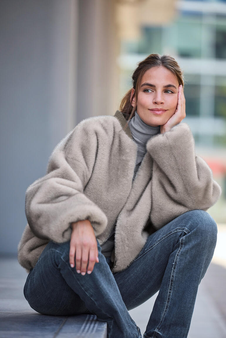 Veste bomber en fausse fourrure beige, portée nonchalamment sur les épaules