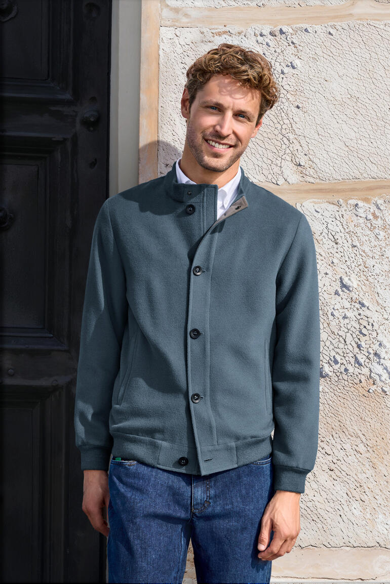 Homme portant un blouson en alpaga brossé bleu devant un mur.