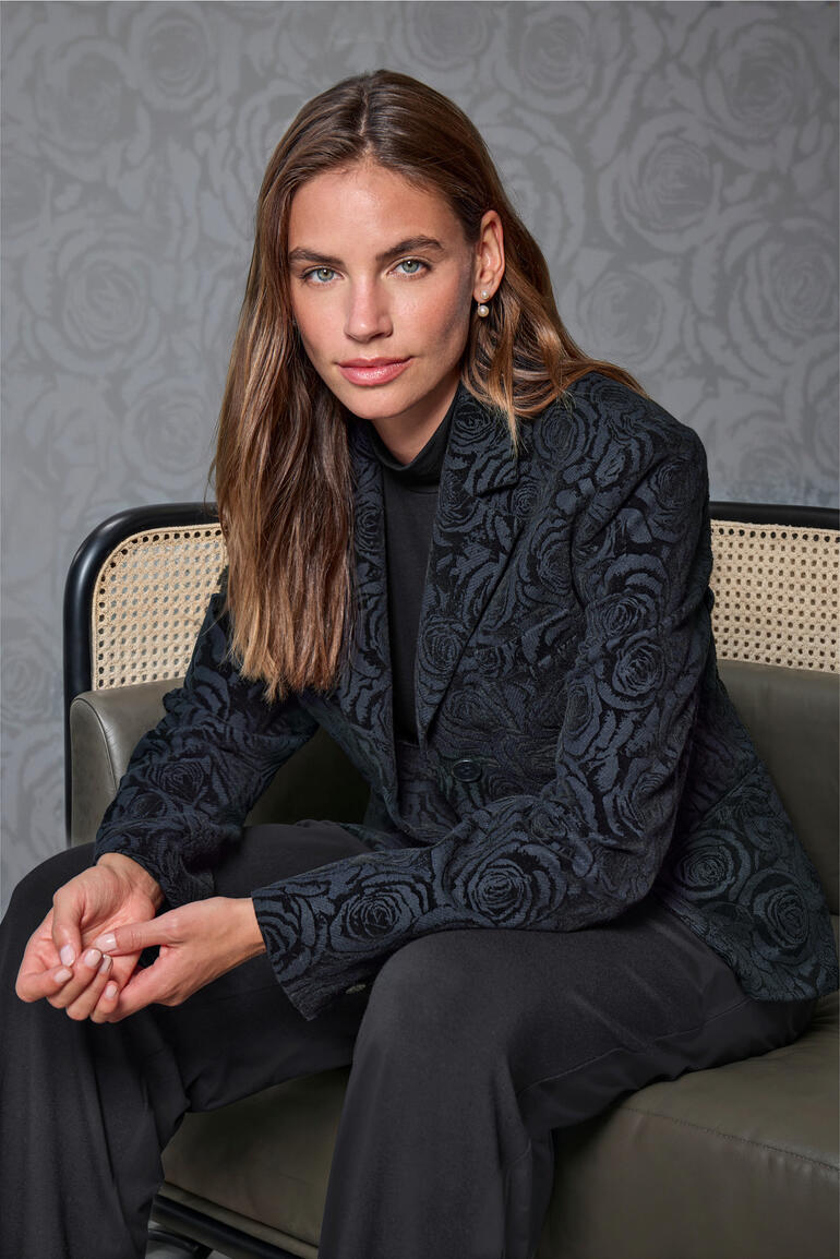 Blazer en flanelle à motif roses Femme en blazer brodé de fleurs assise dans une pièce élégante.