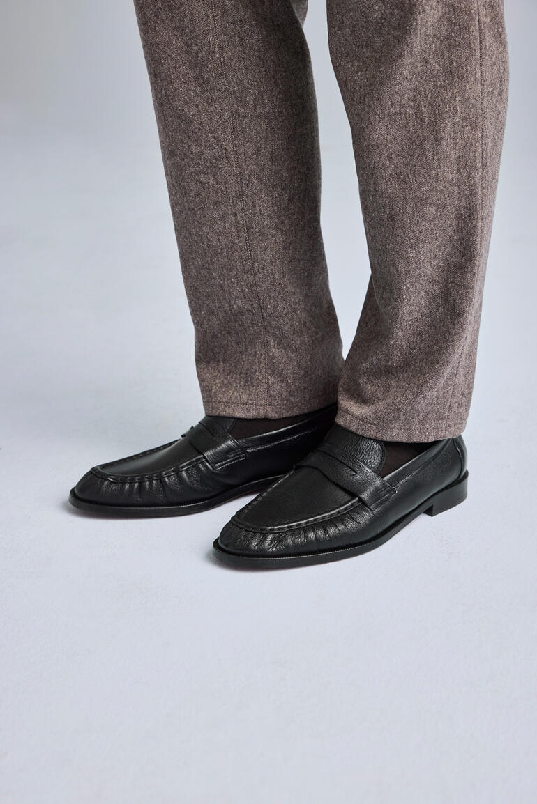 Mocassins noirs élégants avec un pantalon gris au premier plan.
