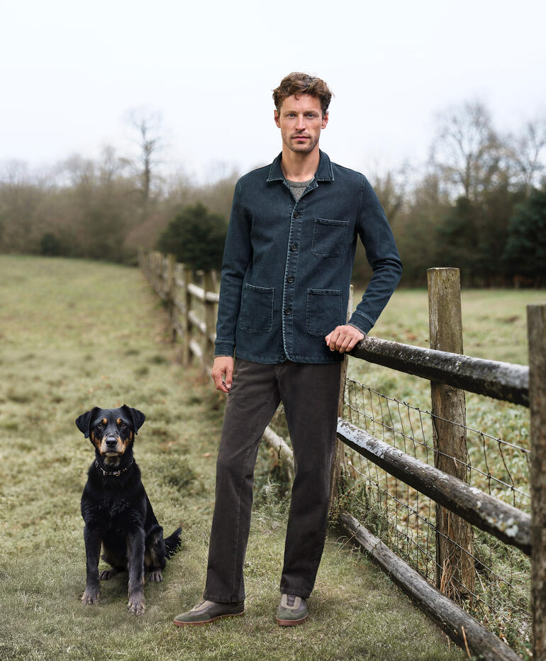Homme portant une veste en denim en cachemire se tenant à côté d'un chien dans un champ.