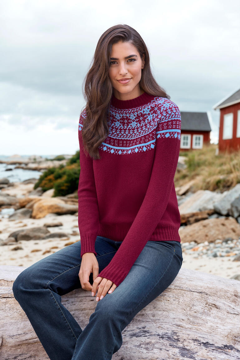 Femme portant un pull Fair-Isle rouge avec motif bleu au bord de la mer.