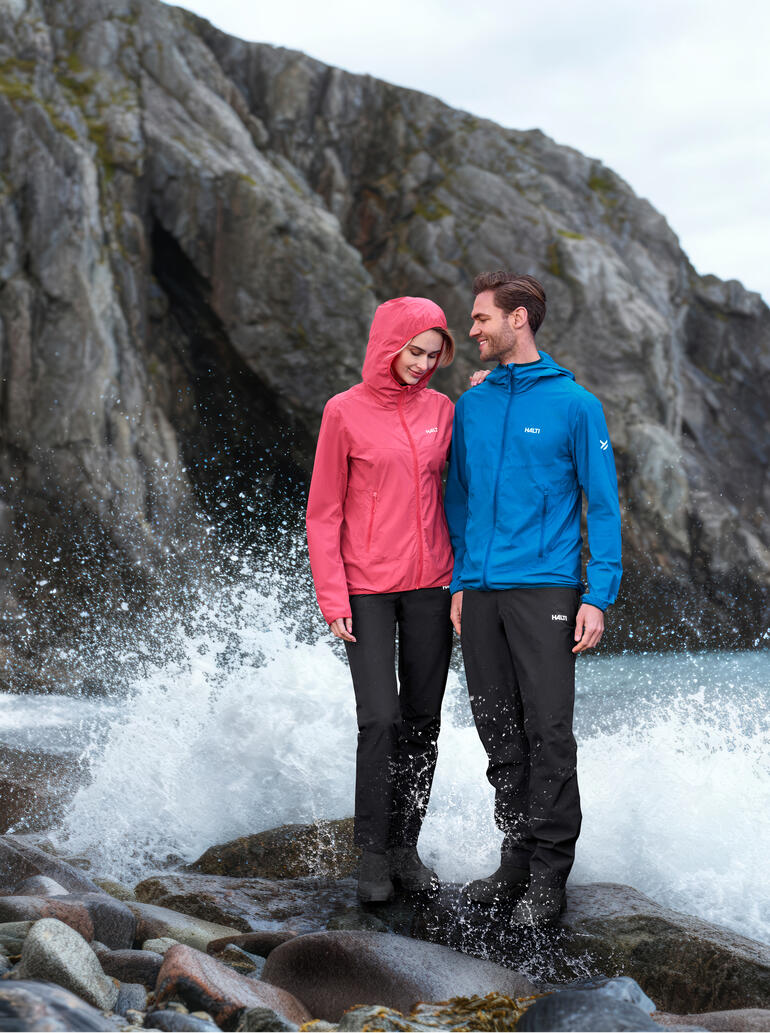 Couple en vêtements d'extérieur, une personne porte une veste softshell rose, l'autre en veste bleue à côté d'une eau agitée.