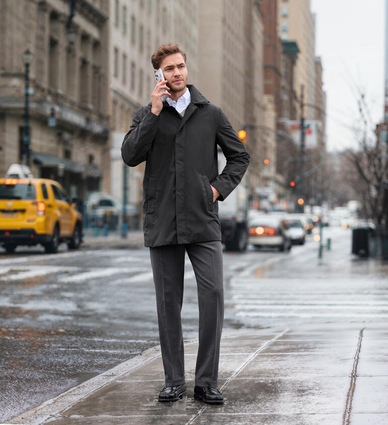 Homme en veste imperméable anthracite tenant un téléphone à son oreille dans un environnement urbain.