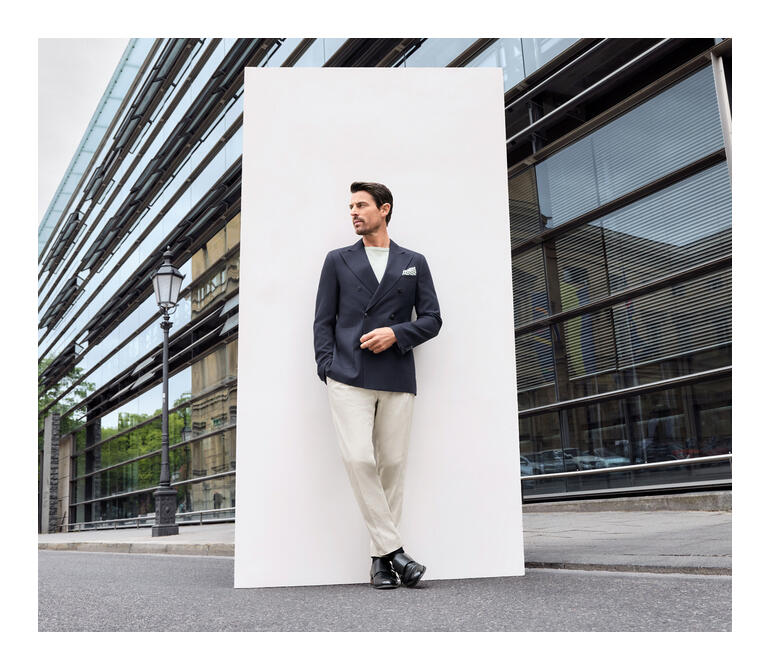 Homme en blazer bleu et pantalon beige posant sur le trottoir.