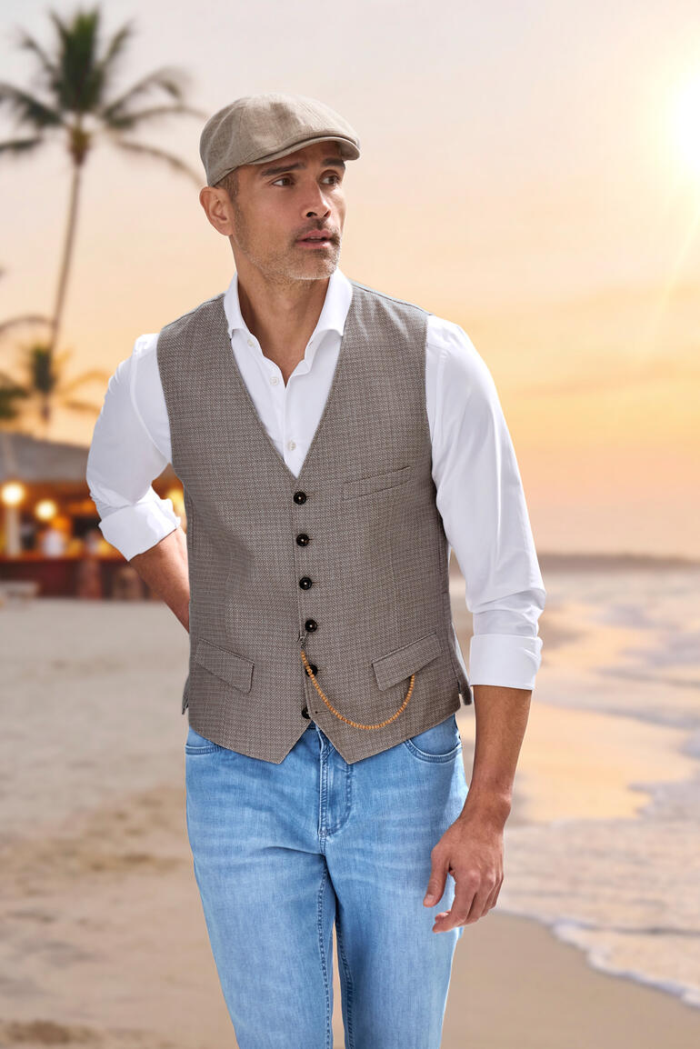 Homme en gilet brun clair et chemise blanche sur la plage au coucher du soleil.