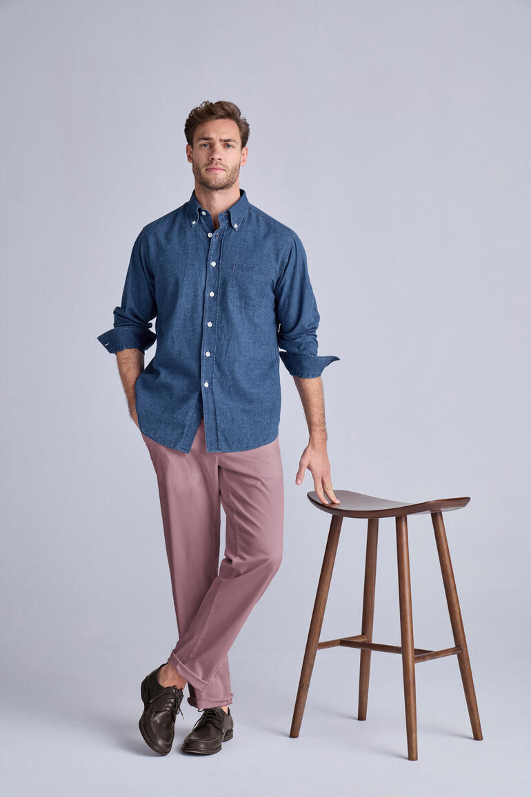 Chemise Ingram en lin et denim bleu, portée de manière décontractée sur un pantalon, chaise en bois en arrière-plan