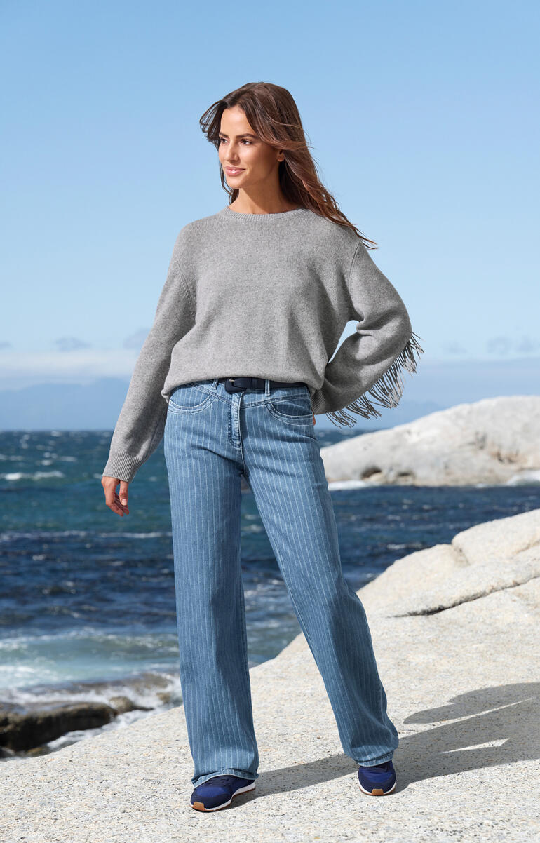 Pull gris à franges, porté décontracté sur un jean à la plage.