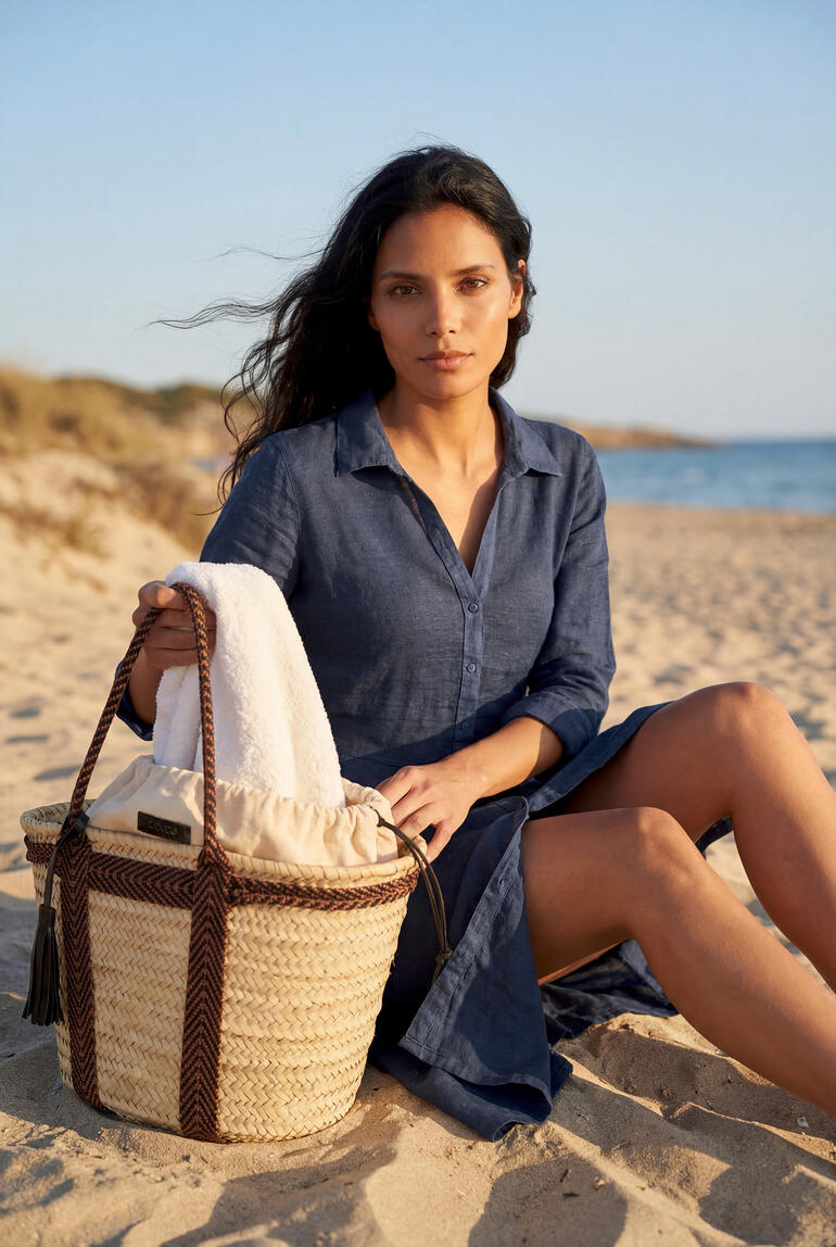 Robe combinée en lin bleu foncé, assise dans le sable avec un sac