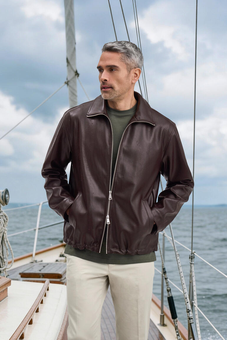 Homme en veste en cuir synthétique marron avec un pull gris sur le pont d'un voilier