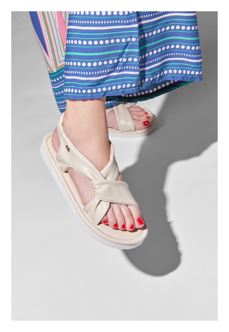 Pieds dans des sandales ultralégères vanille, jupe en tissu en arrière-plan.