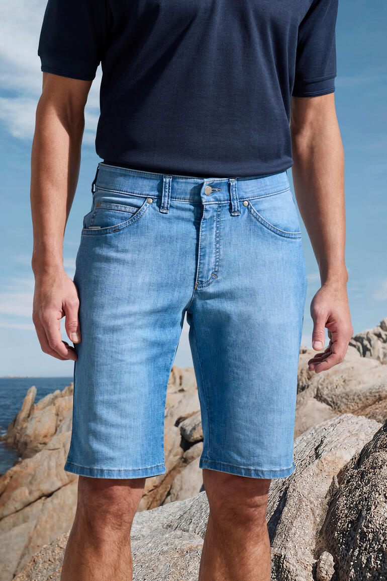 Homme en shorts en jeans clairs sur des rochers en bord de mer