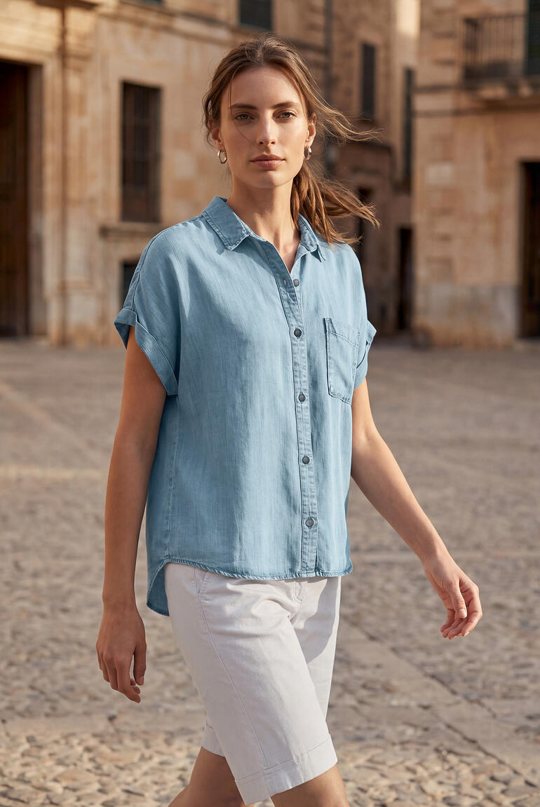 Femme en chemisier en denim doux à manches courtes bleu marchant avec assurance dans une rue.