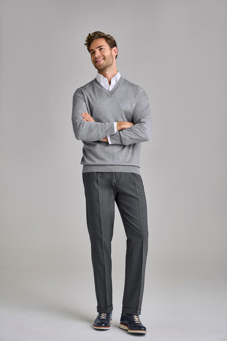 Pantalon gris à plis pour hommes, debout avec un pull.