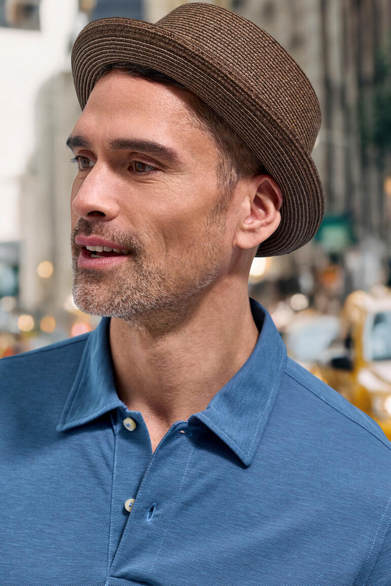 Homme portant un chapeau Pork Pie marron et un polo bleu.