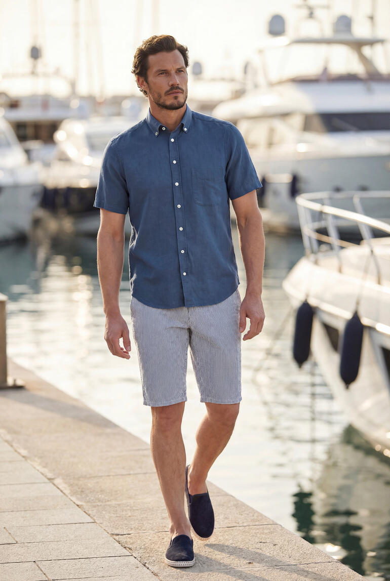 Homme en chemise BDO marine et shorts marchant le long du port.