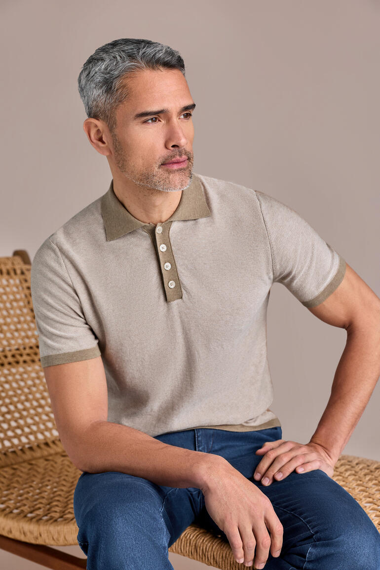Homme portant un polo beige sable avec boutons, assis sur une chaise.