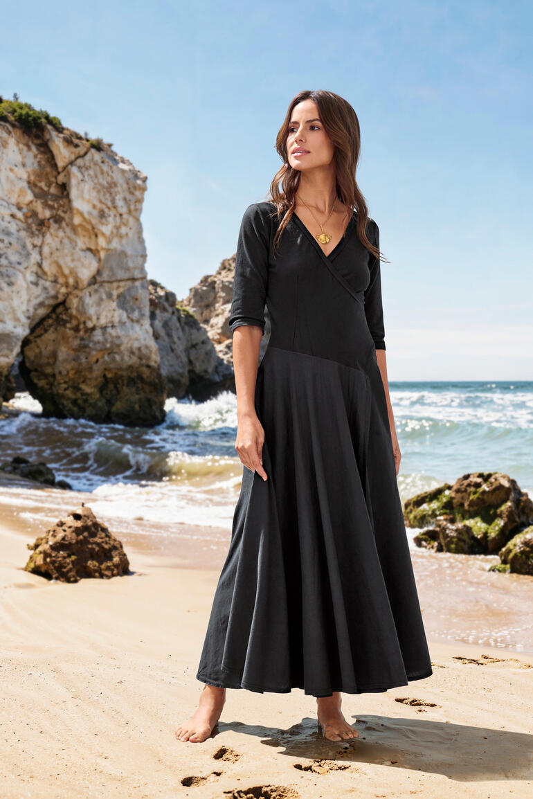 Femme en robe Ibiza noire se tenant sur la plage.