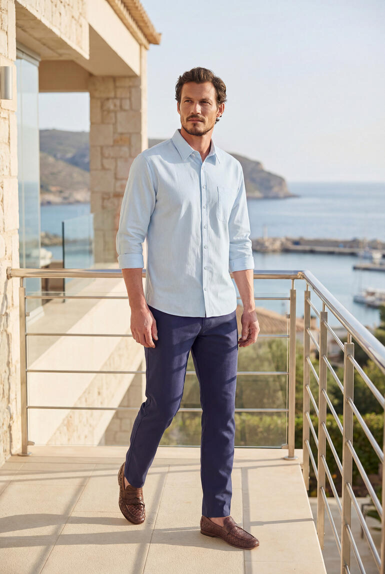 Homme en chemise seersucker bleu clair et pantalon marine se tenant sur un balcon.