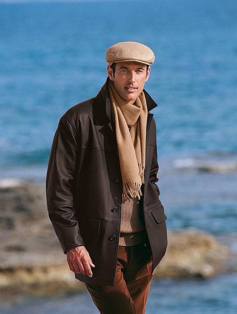 Homme portant une casquette en poil de chameau et une écharpe, regardant la mer.