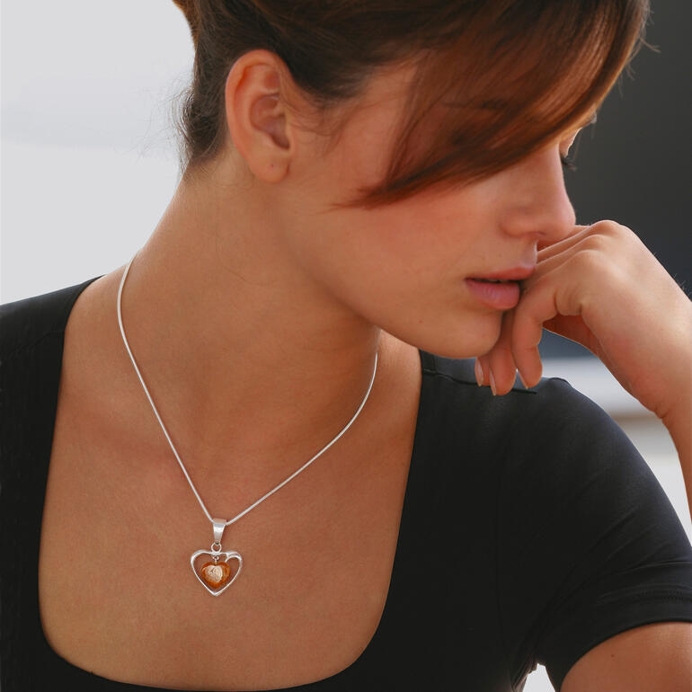 Collier en forme de cœur en ambre porté par une femme pensive, main sur le menton