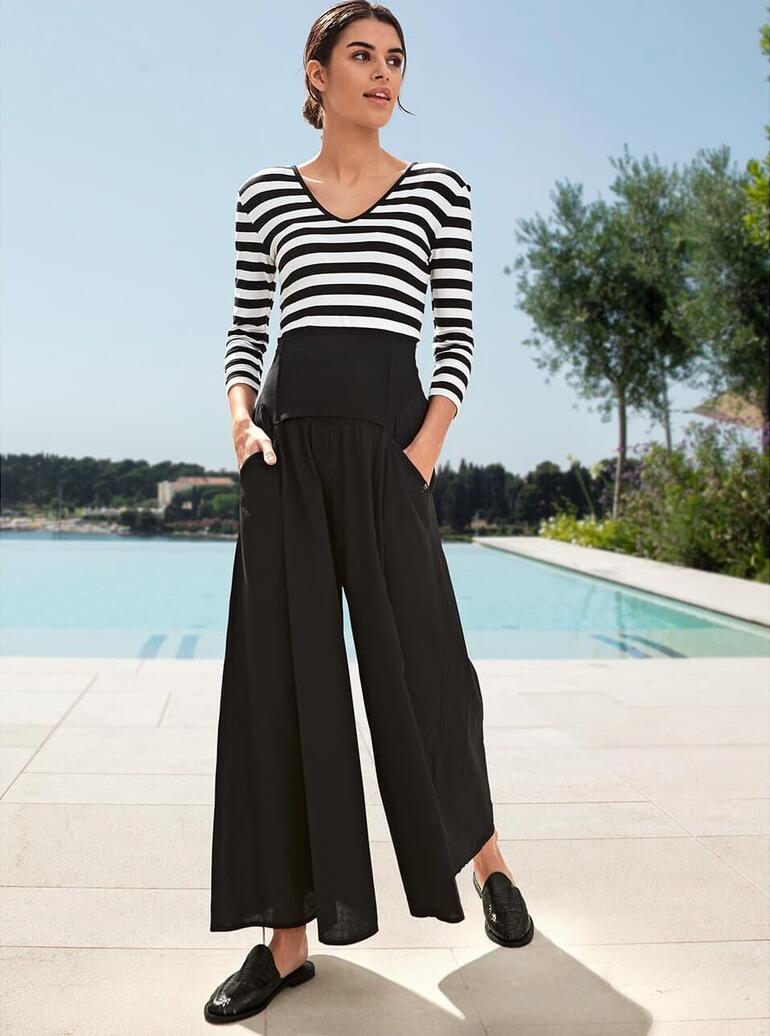 Jupe-culotte Ibiza Elisa F. Femme portant un t-shirt magique rayé avec un pantalon noir, debout devant une piscine.