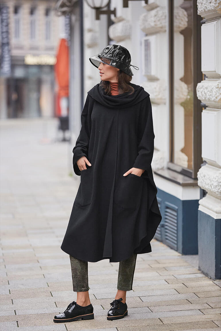 Modèle féminin portant un manteau cape noir, debout dans la ville.