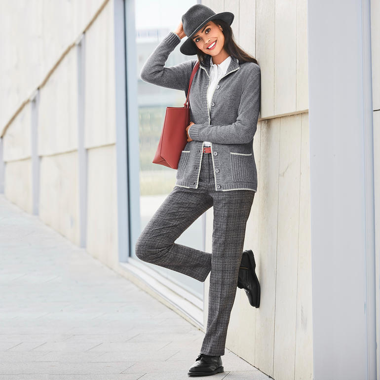 Gris chiné Femme en cardigan en cachemire gris avec un chapeau noir et un sac rouge, s'appuyant contre un mur.