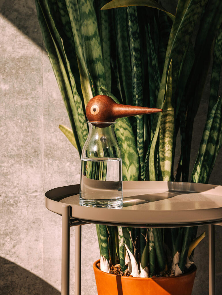 Vase en verre avec un distributeur d'eau en bois en forme d'oiseau sur une table.