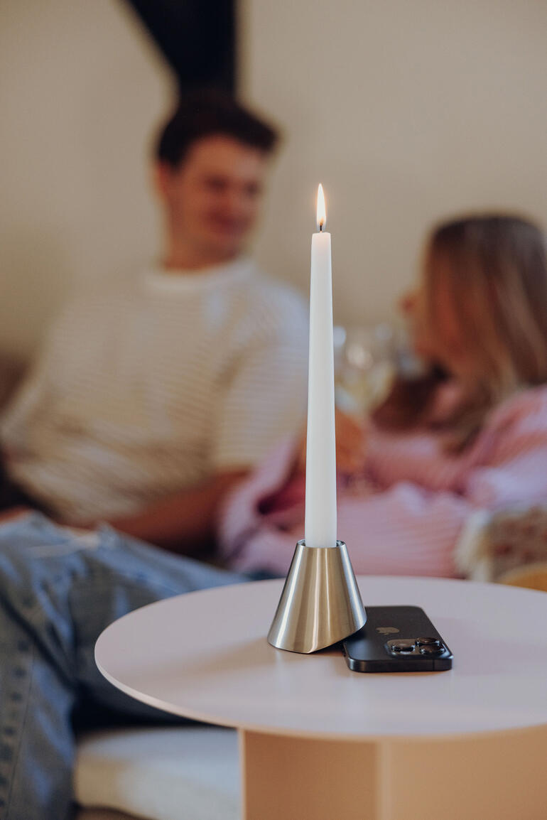 Bougie dans un support en métal sur une table, arrière-plan avec des personnes.