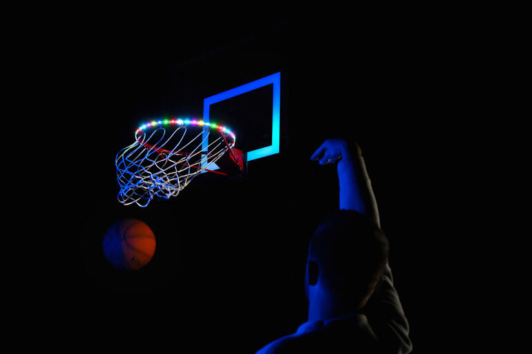 Panier de basket-ball avec lumières LED colorées et personne lançant sur un terrain sombre.