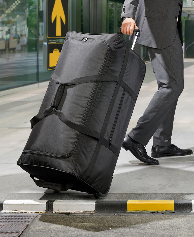 Un sac de voyage ultraléger XXL noir est poussé par un homme en costume.