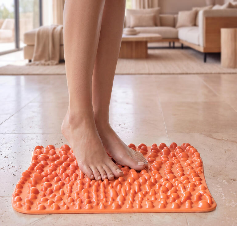 Mat de réflexologie plantaire goFit en orange vif, sur un sol clair avec des pieds dessus.