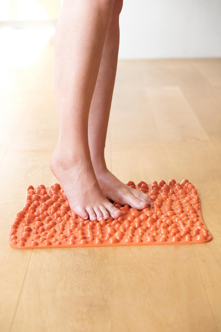 Mat de réflexologie plantaire goFit en orange vif, pieds dessus.