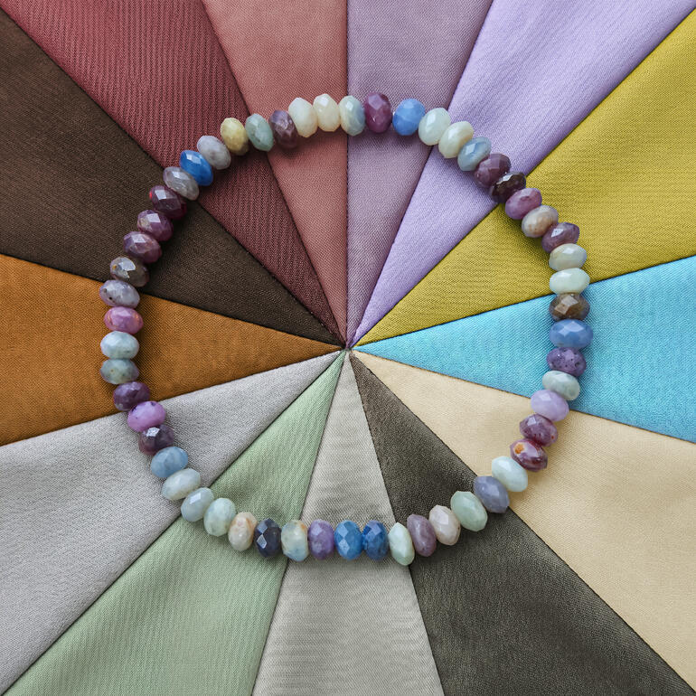 Collier de perles Chamäleon colorées devant un fond de tissus de différentes couleurs.