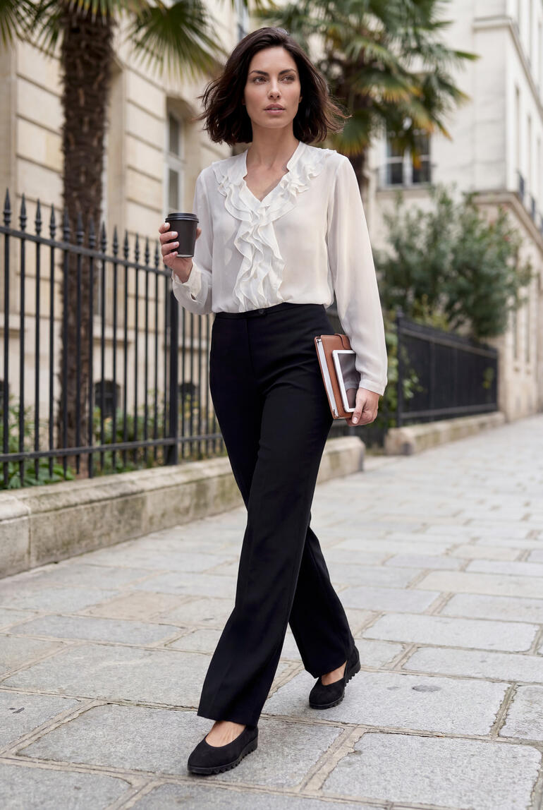 Femme en pantalon de valise et blouse tenant un gobelet de café en marchant