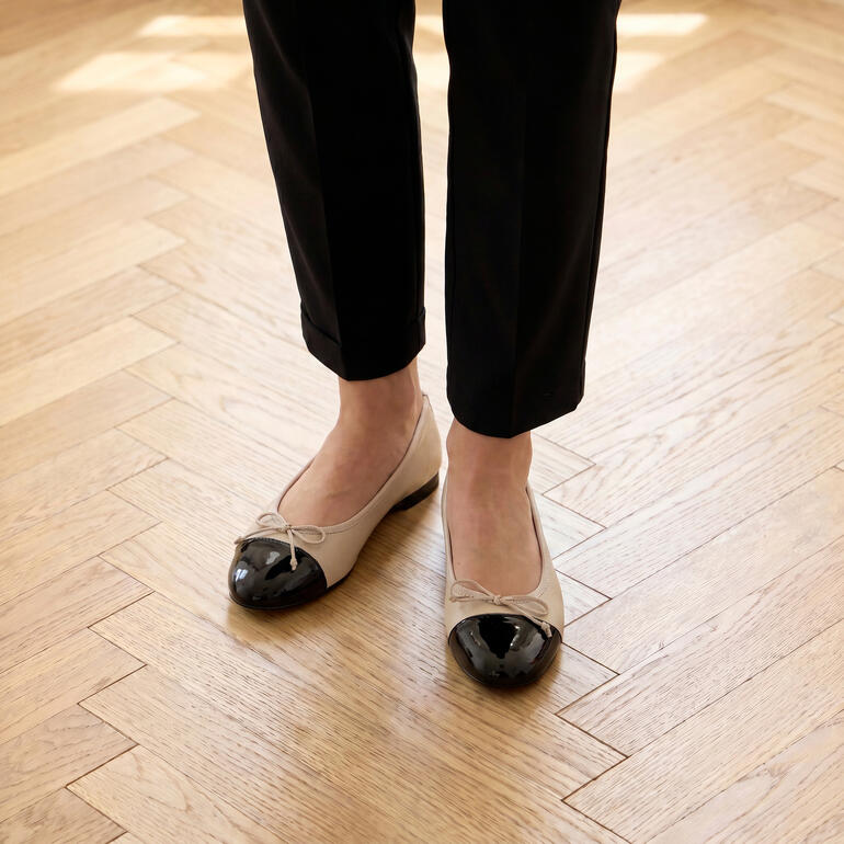 Ballerines beiges avec une zone noire sur un sol en bois