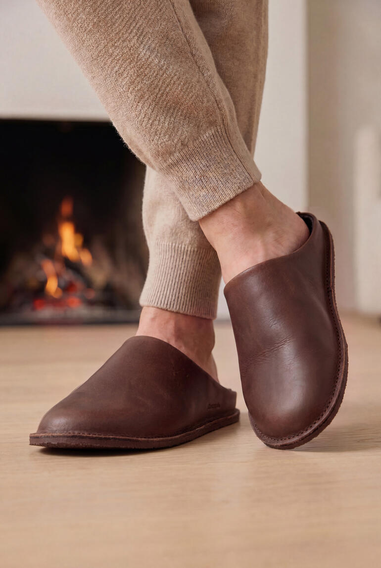 Chaussons en cuir marron aux pieds d'une personne devant une cheminée