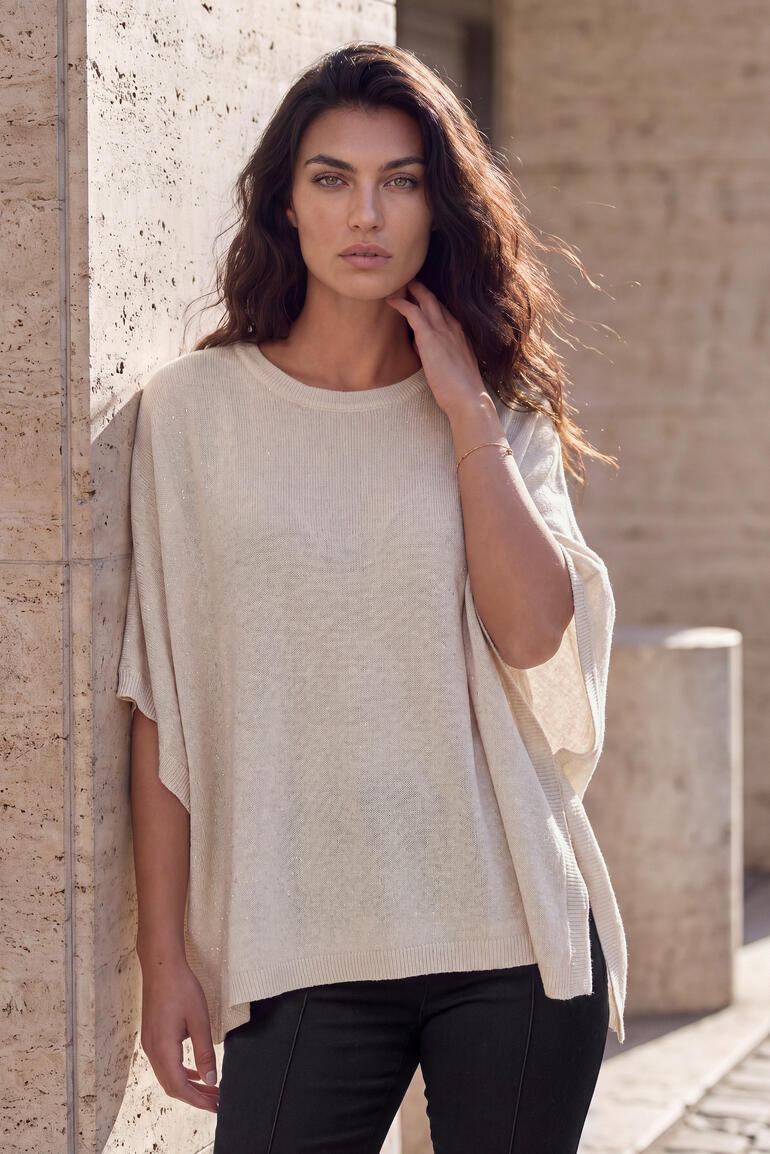 Femme dans un poncho en cachemire glamour beige devant un mur