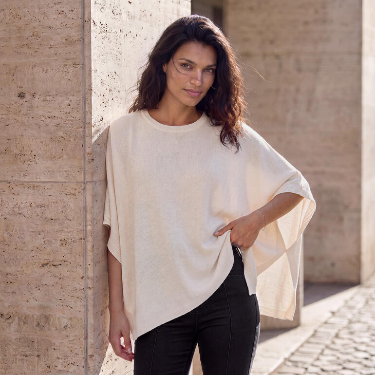 Femme portant un poncho glamour en cachemire beige contre un mur