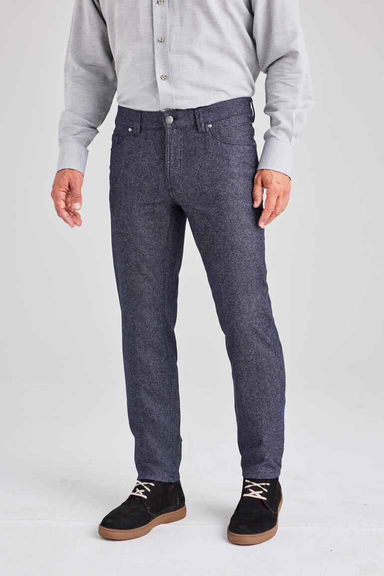 Homme en chemise grise et jeans en laine se tient devant un fond clair