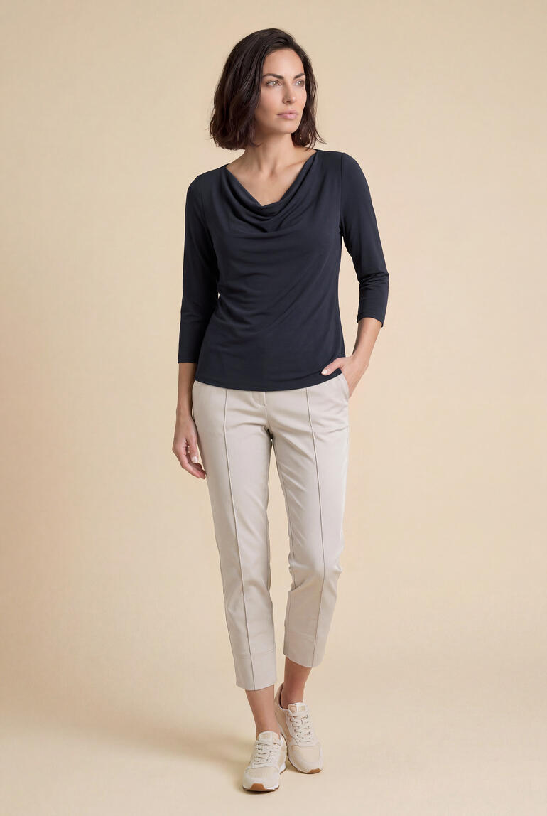 Femme portant un t-shirt à col en cascade en modal micro avec un pantalon clair devant un fond beige