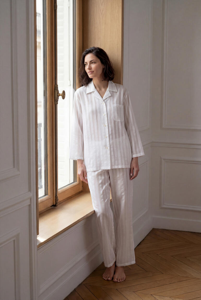 Femme en pyjama rayée en coton soie se tient élégamment devant la fenêtre