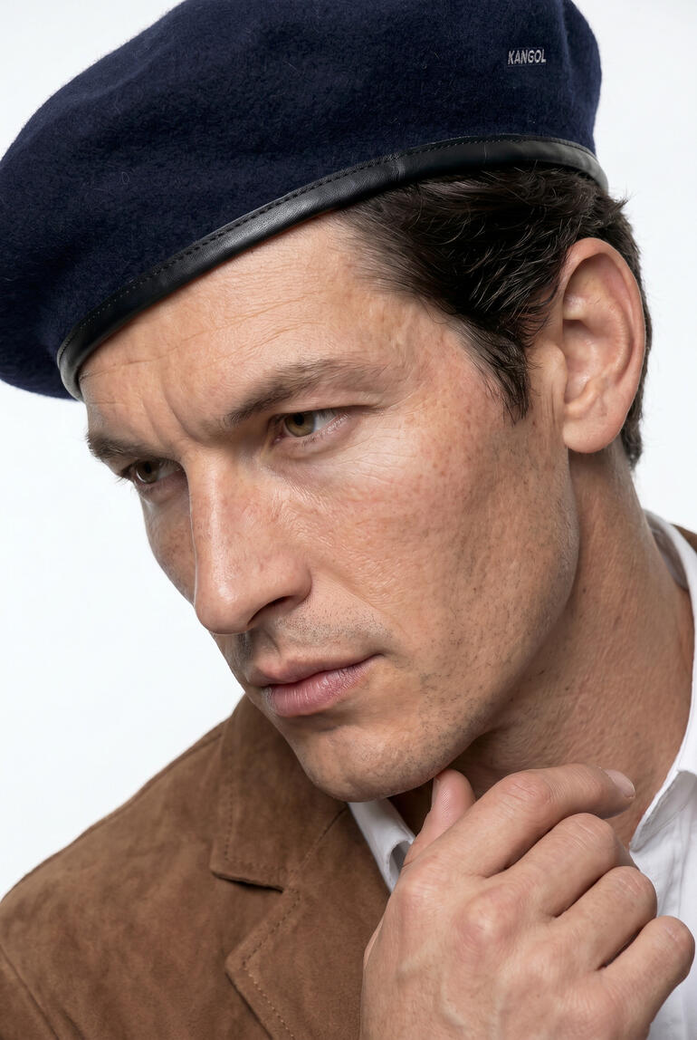 Homme portant un béret Kangol et regardant pensivement.