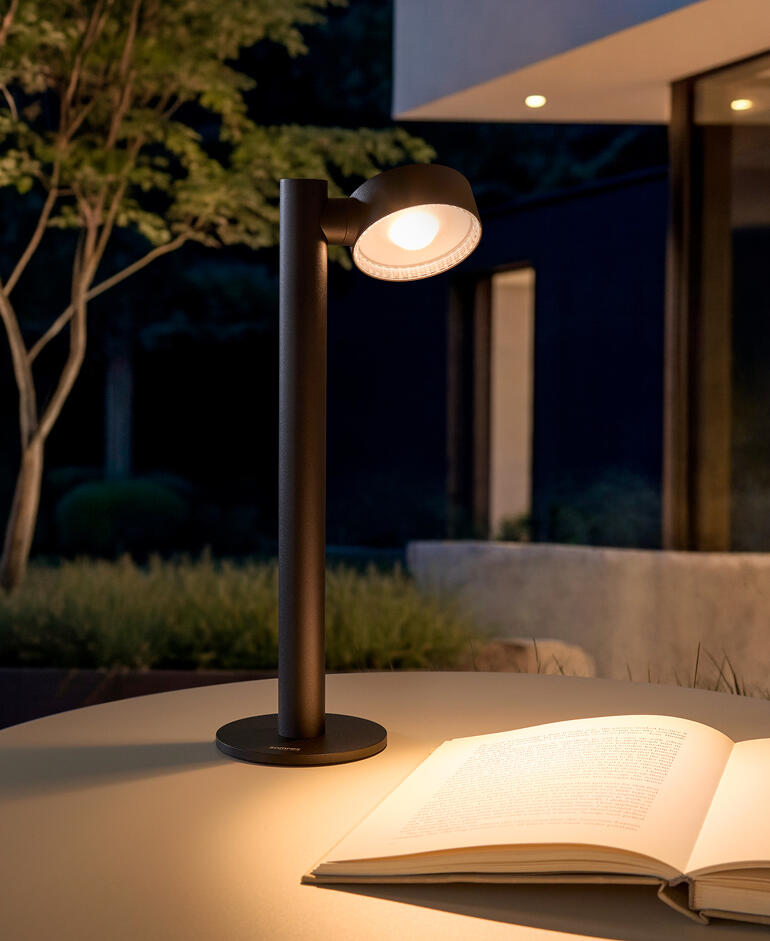 Lampe de table à batterie sur une table à l'extérieur, avec un livre à côté.