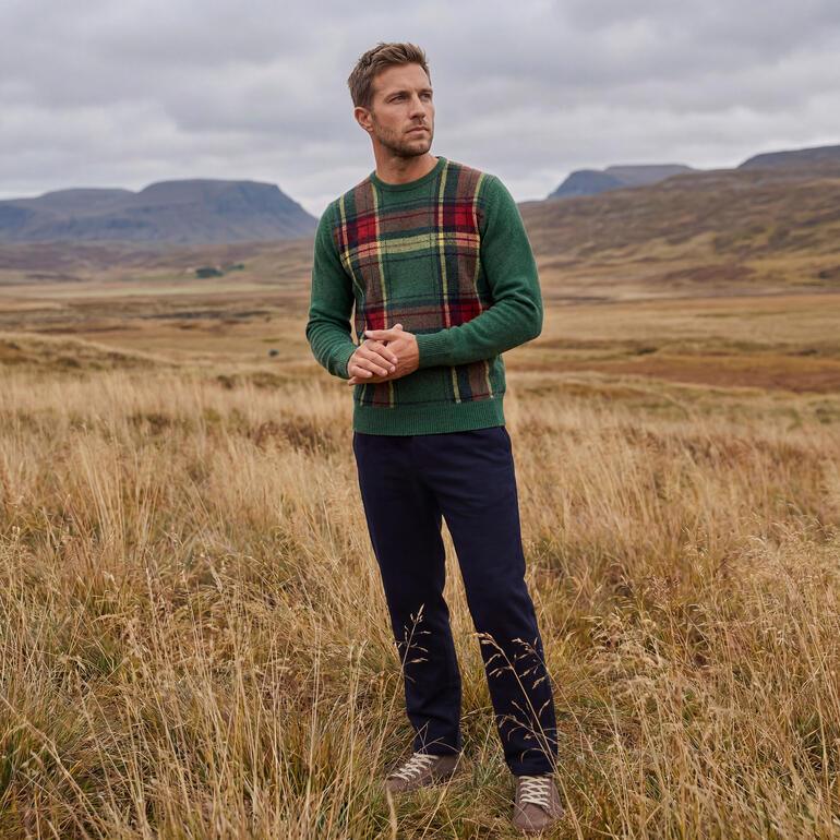 Homme en pull tartan vert se tient dans un paysage automnal.